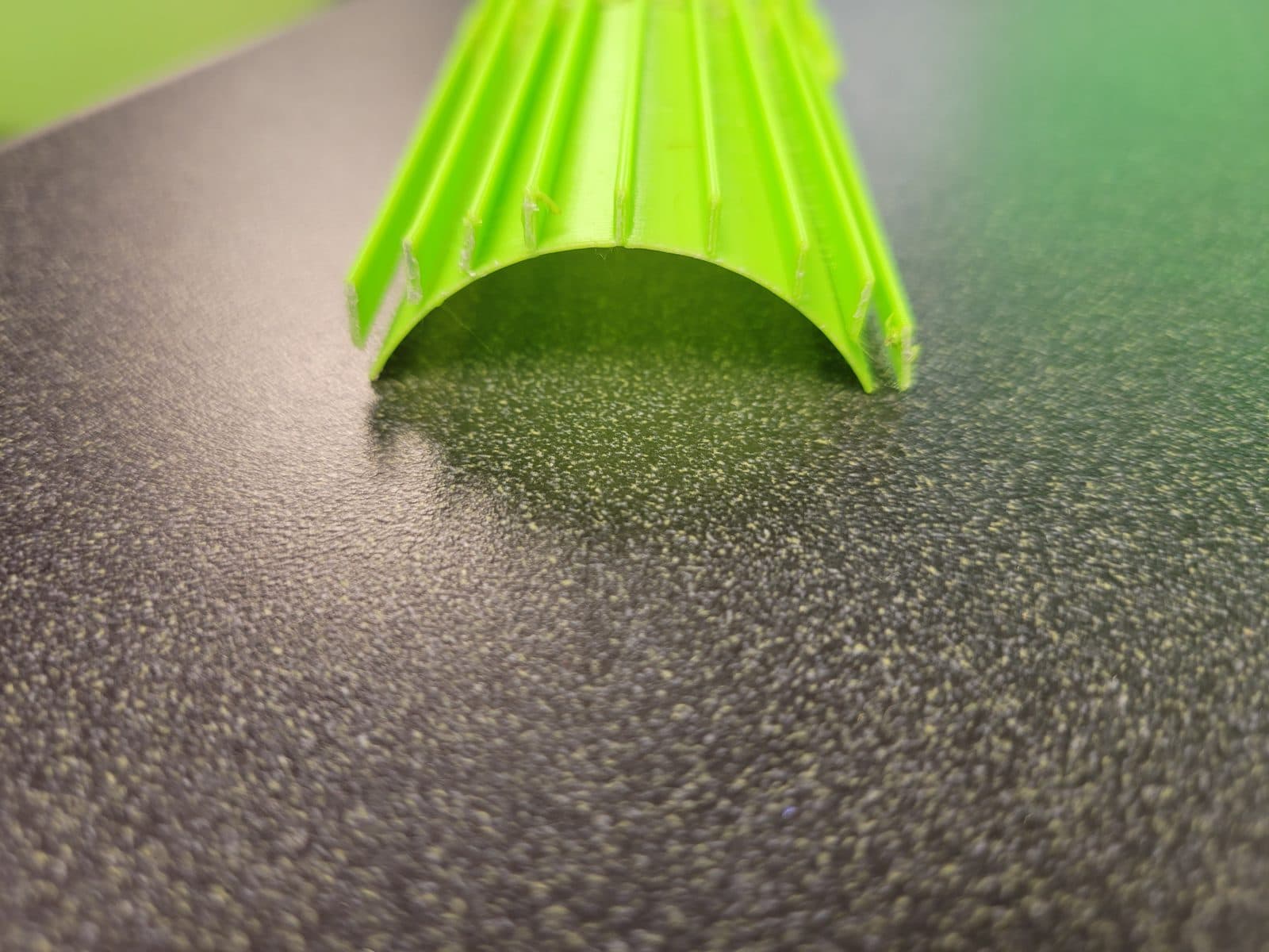 End view of a green ribbed form with an arched cross-section, resting on a dark surface