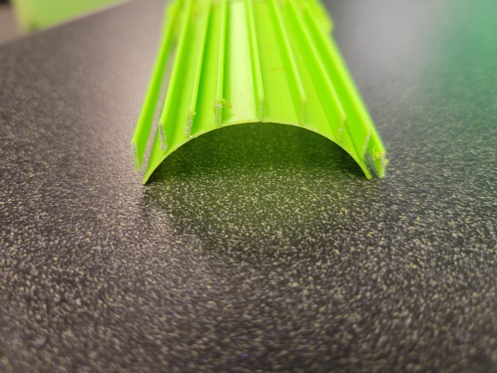 Close-up of the open end of a green ribbed arch form, showing the curved shell and rib edges