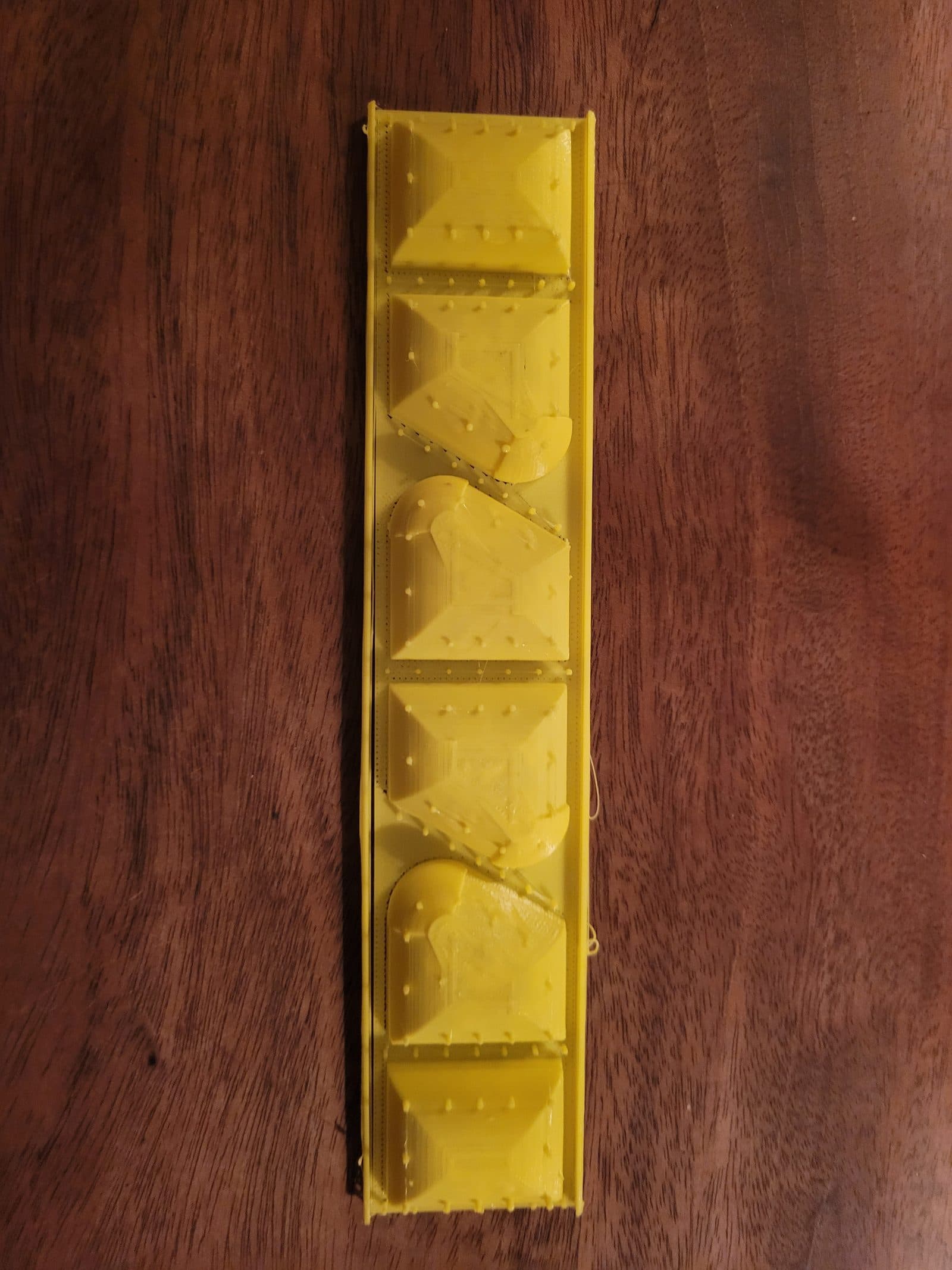 Top view of a long yellow form tray holding a row of raised pyramid- and dome-shaped sections