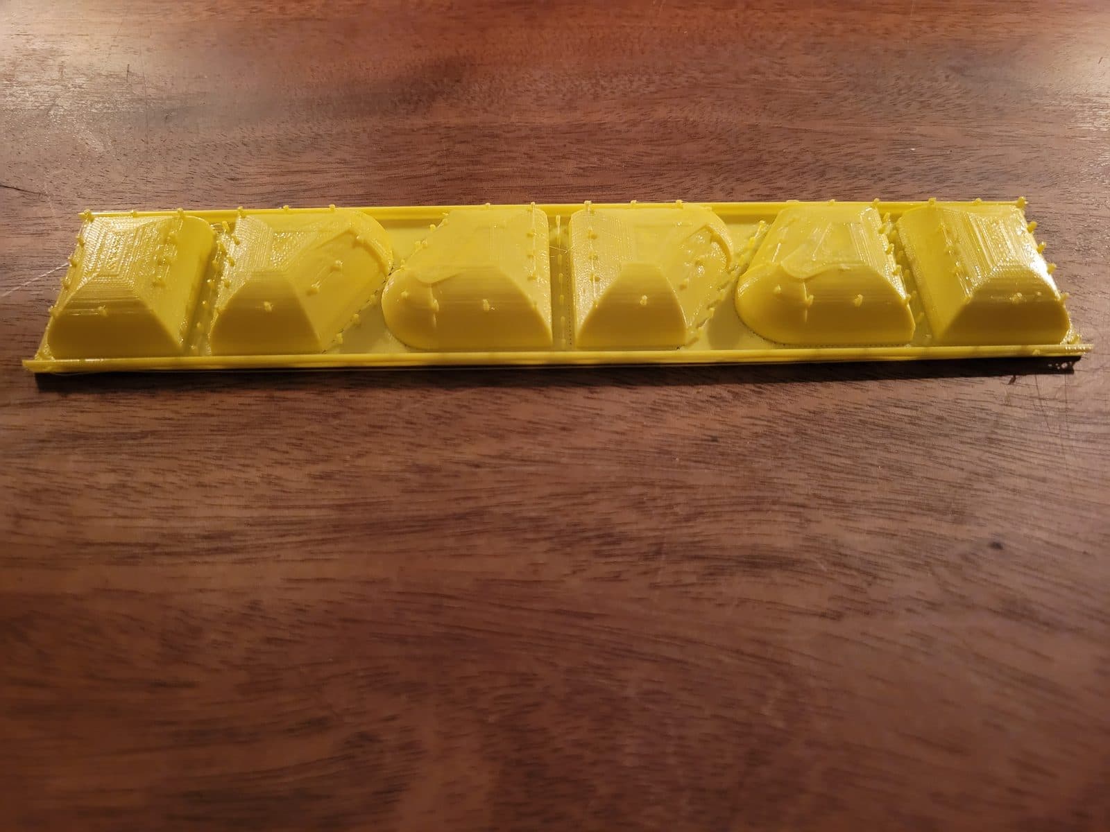 Side view of the yellow form tray showing six raised trapezoidal and domed sections in a row