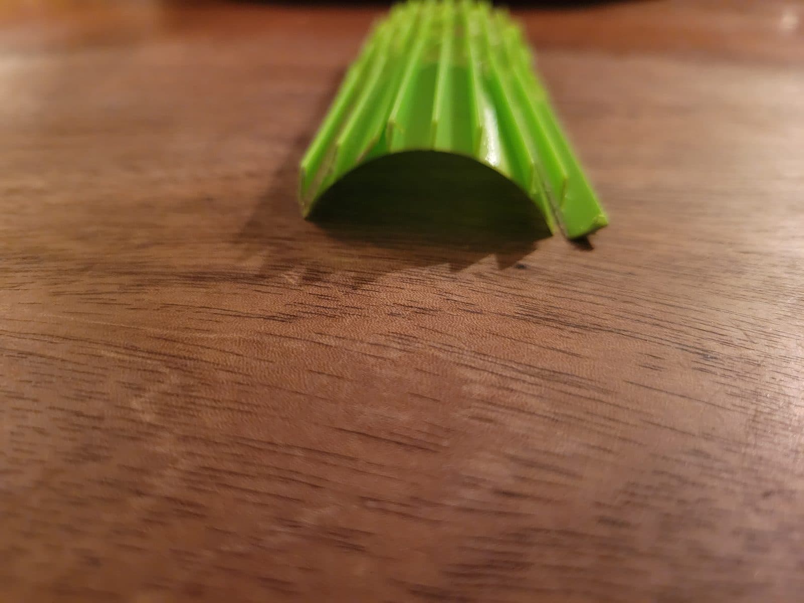 Green arched form with longitudinal ribs on a wooden table, seen from one end